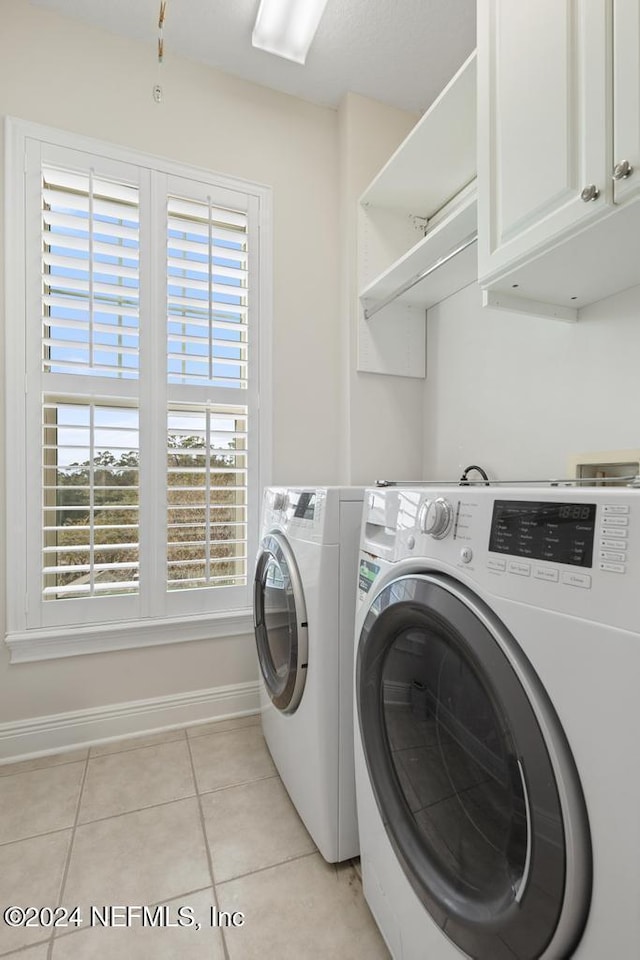 clothes washing area with washer and clothes dryer, cabinets, and light tile patterned floors