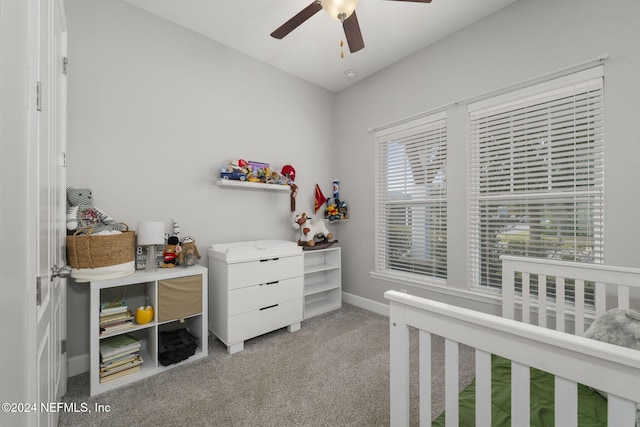 carpeted bedroom with a crib and ceiling fan