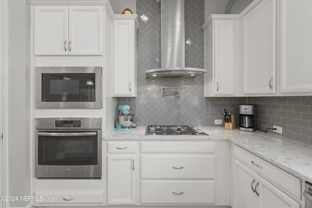 kitchen with white cabinets, appliances with stainless steel finishes, backsplash, and wall chimney exhaust hood