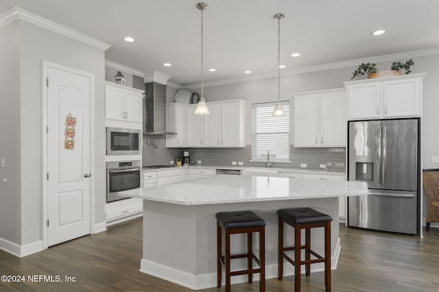 kitchen with white cabinets, appliances with stainless steel finishes, a center island, and wall chimney range hood