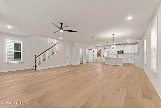 unfurnished living room featuring a barn door, a wealth of natural light, ceiling fan, and light hardwood / wood-style floors