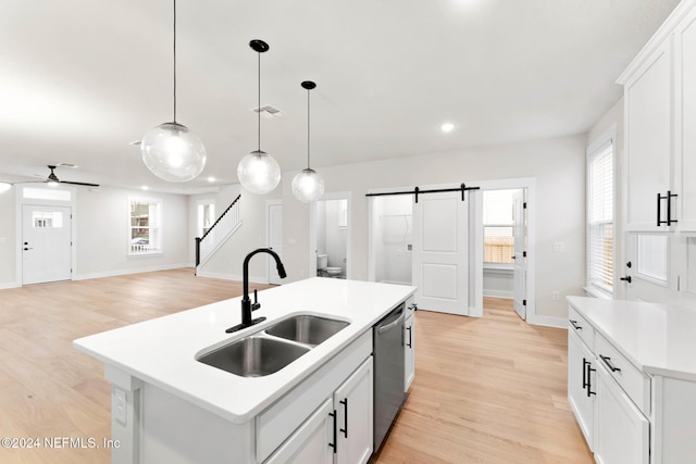 kitchen featuring sink, dishwasher, a barn door, light hardwood / wood-style floors, and a kitchen island with sink