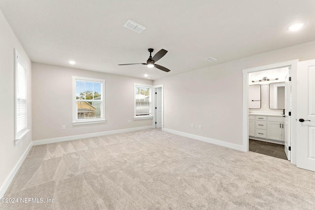 unfurnished bedroom featuring light colored carpet, ensuite bath, and ceiling fan