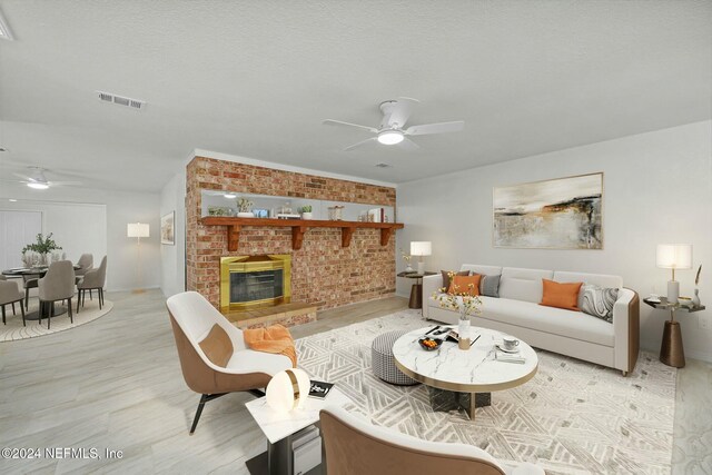 living room featuring brick wall, a textured ceiling, ceiling fan, light hardwood / wood-style flooring, and a fireplace