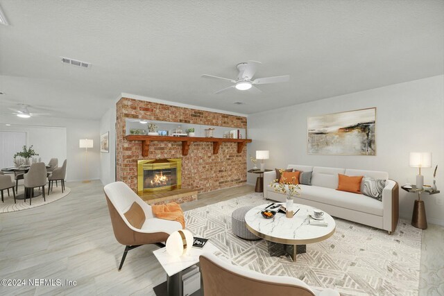 living room with ceiling fan, brick wall, a textured ceiling, a fireplace, and light wood-type flooring