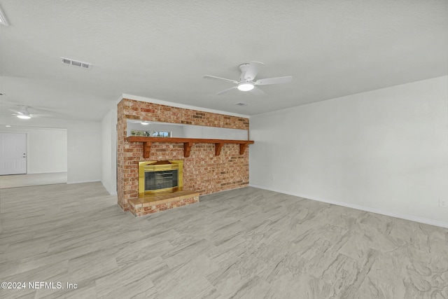 unfurnished living room with ceiling fan, a large fireplace, brick wall, and a textured ceiling