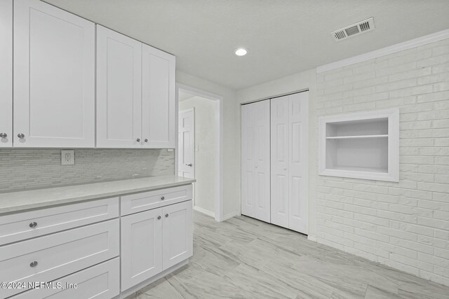 kitchen featuring tasteful backsplash, white cabinets, and brick wall