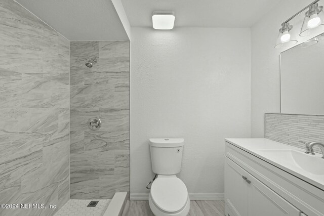 bathroom featuring tiled shower, vanity, toilet, and backsplash