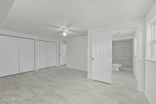 unfurnished bedroom featuring a textured ceiling, ensuite bath, ceiling fan, and multiple closets