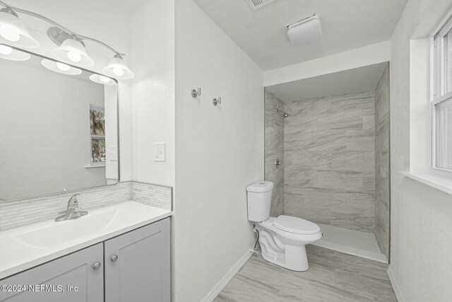 bathroom featuring a tile shower, vanity, and toilet