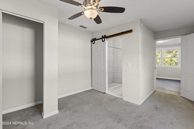 unfurnished bedroom with carpet, ceiling fan, and a barn door