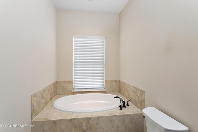 bathroom with a relaxing tiled tub, toilet, and a textured ceiling