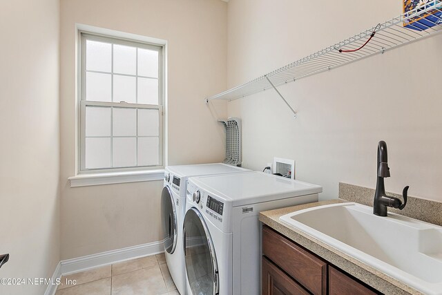 clothes washing area with washing machine and dryer, sink, light tile patterned floors, and cabinets