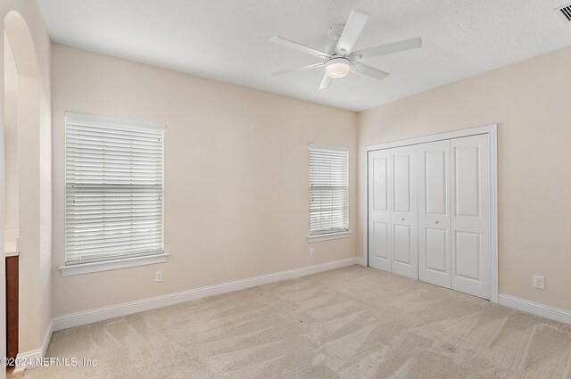 unfurnished bedroom featuring ceiling fan, light colored carpet, a textured ceiling, and a closet