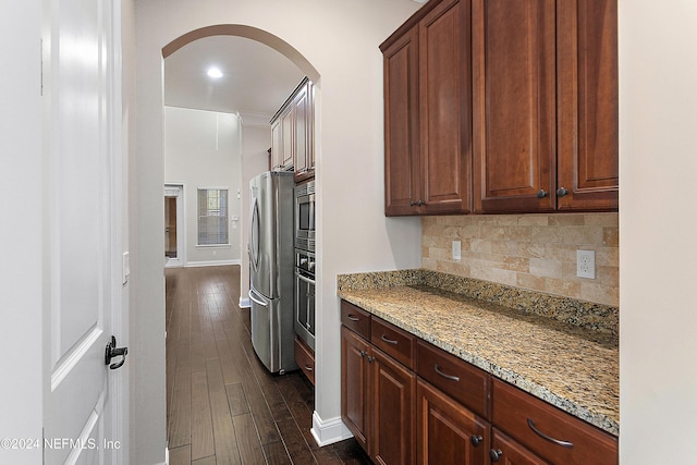 kitchen with light stone countertops, dark hardwood / wood-style flooring, stainless steel appliances, and backsplash