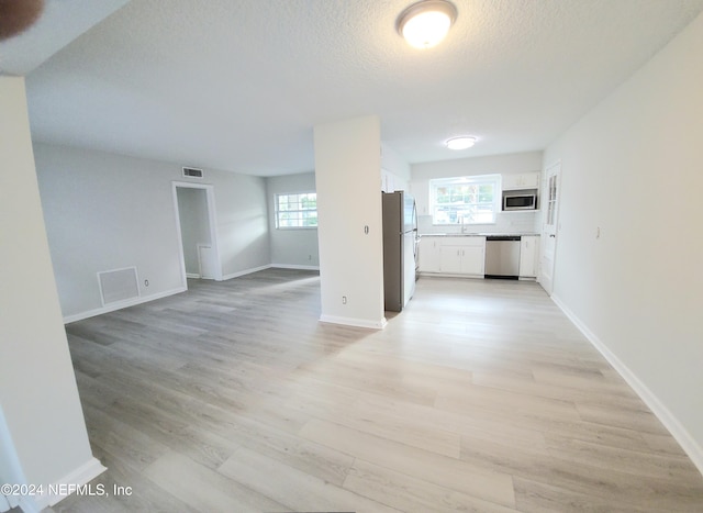 unfurnished living room featuring a textured ceiling, light wood-type flooring, a healthy amount of sunlight, and sink