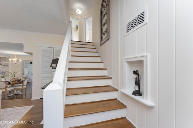 staircase featuring crown molding, an inviting chandelier, and hardwood / wood-style flooring