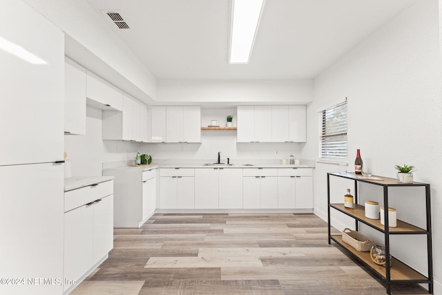 kitchen with light hardwood / wood-style floors, white cabinetry, white fridge, and sink