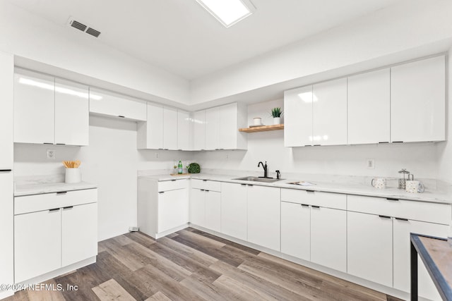 kitchen with light wood-type flooring, white cabinetry, and sink