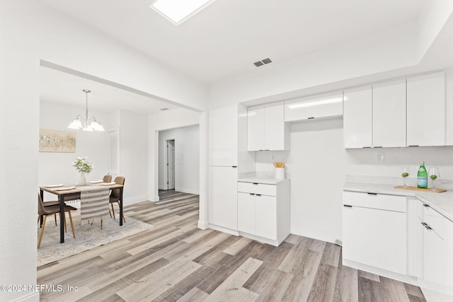 kitchen with pendant lighting, light hardwood / wood-style floors, white cabinetry, and an inviting chandelier