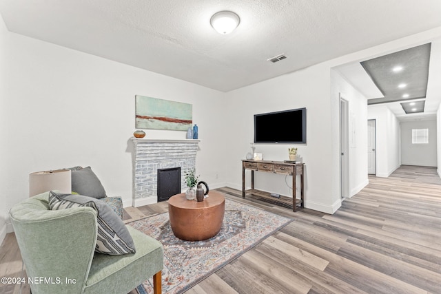 living room with a fireplace, a textured ceiling, and light hardwood / wood-style flooring