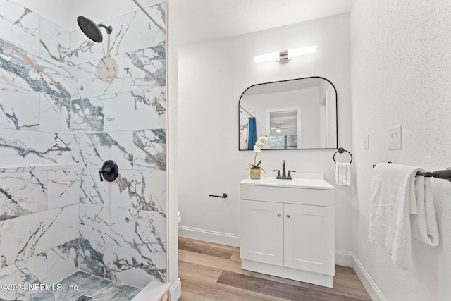 bathroom with a tile shower, hardwood / wood-style floors, vanity, and toilet