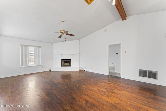 unfurnished living room featuring ceiling fan, beamed ceiling, a brick fireplace, and dark hardwood / wood-style flooring