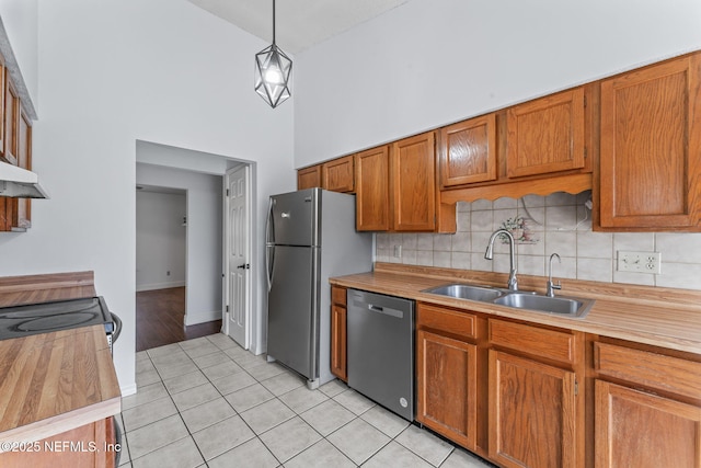 kitchen featuring appliances with stainless steel finishes, hanging light fixtures, light tile patterned floors, sink, and high vaulted ceiling