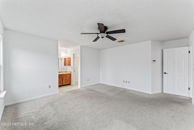 interior space featuring ceiling fan, light colored carpet, a textured ceiling, and ensuite bath