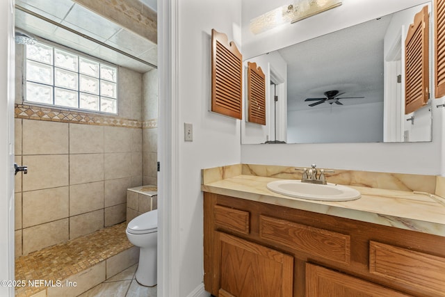 bathroom with toilet, tile patterned floors, tiled shower, vanity, and ceiling fan