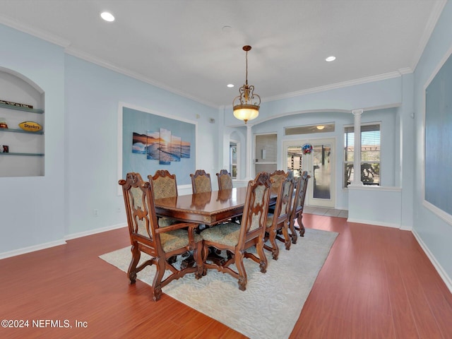 dining area featuring built in features, wood-type flooring, crown molding, and decorative columns