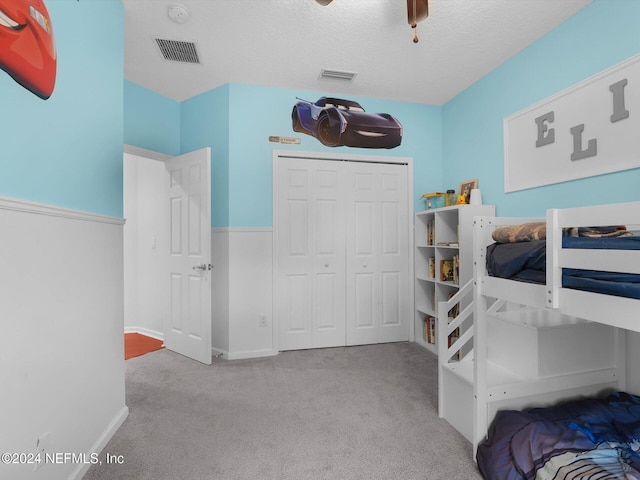 bedroom with ceiling fan, light colored carpet, a textured ceiling, and a closet