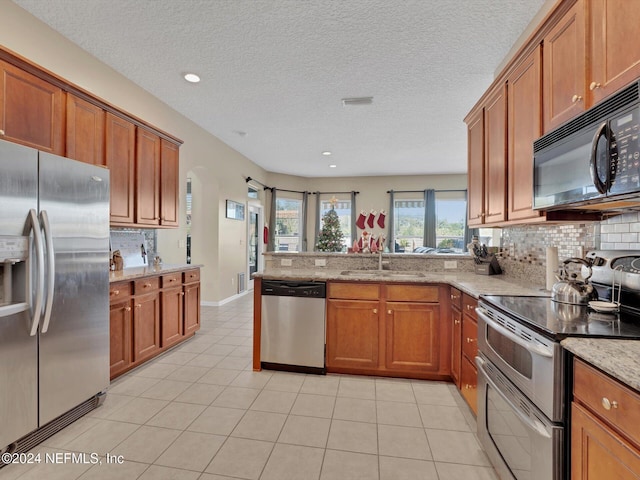 kitchen featuring sink, light stone counters, backsplash, kitchen peninsula, and appliances with stainless steel finishes