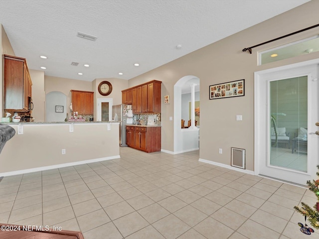 kitchen with kitchen peninsula, stainless steel fridge, tasteful backsplash, a textured ceiling, and light tile patterned flooring