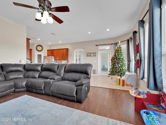 living room with ceiling fan, light wood-type flooring, and a textured ceiling