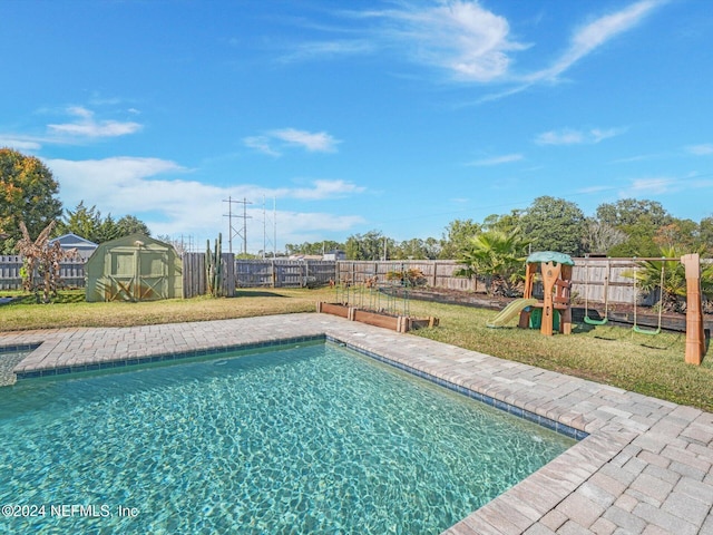 view of swimming pool featuring a storage unit, a playground, and a yard