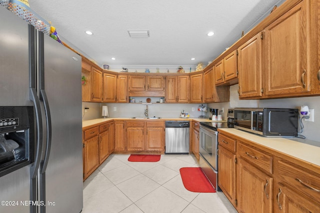 kitchen featuring sink, light tile patterned floors, stainless steel appliances, and a textured ceiling