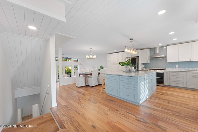 kitchen with wall chimney exhaust hood, light hardwood / wood-style flooring, stainless steel range oven, pendant lighting, and a kitchen island