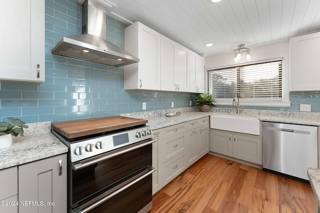 kitchen featuring appliances with stainless steel finishes, light wood-type flooring, white cabinetry, and wall chimney range hood