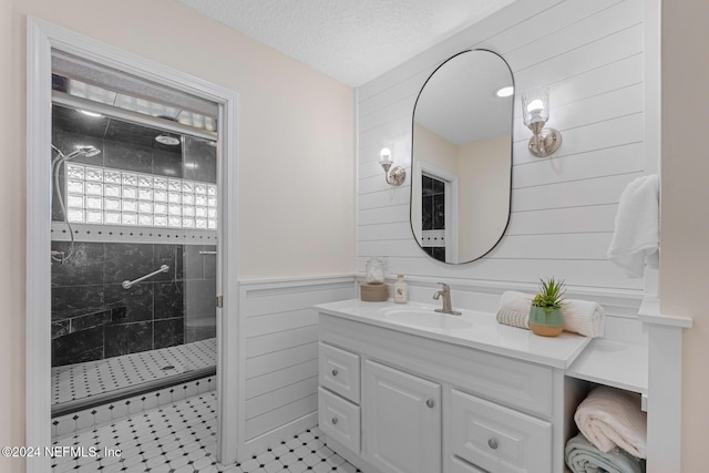 bathroom with a tile shower, tile patterned flooring, a textured ceiling, wooden walls, and vanity