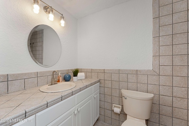 bathroom featuring a textured ceiling, vanity, toilet, and tile walls