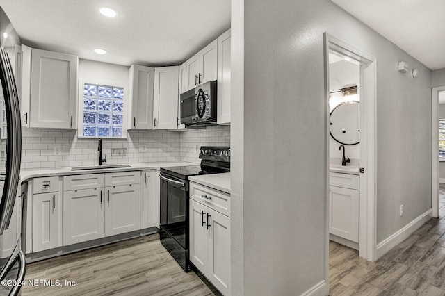 kitchen with black range with electric stovetop, sink, light hardwood / wood-style floors, decorative backsplash, and white cabinets