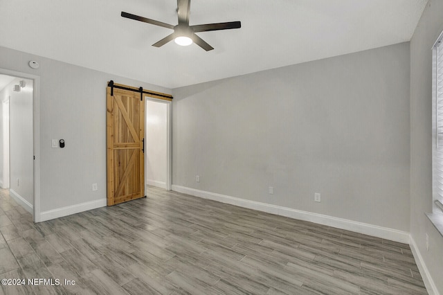 empty room with a barn door, ceiling fan, and light hardwood / wood-style flooring