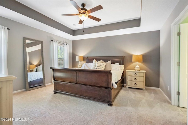 bedroom featuring ceiling fan, a raised ceiling, and light carpet