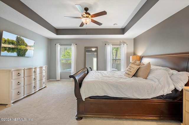 carpeted bedroom with a raised ceiling and ceiling fan