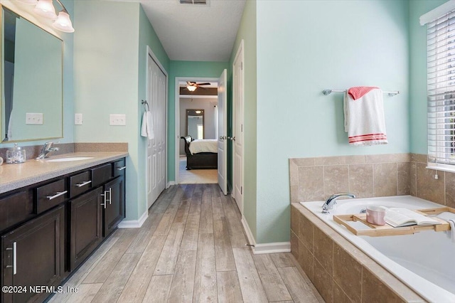 bathroom featuring hardwood / wood-style floors, vanity, a relaxing tiled tub, and ceiling fan