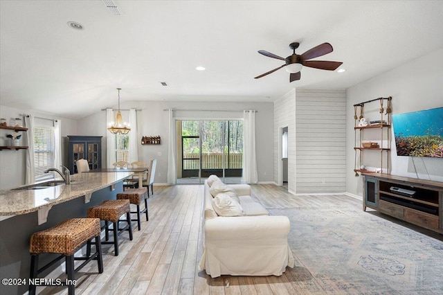 living room with lofted ceiling, sink, ceiling fan with notable chandelier, and light wood-type flooring