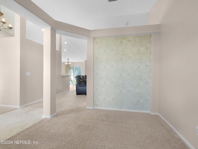 spare room featuring light colored carpet, a textured ceiling, and an inviting chandelier