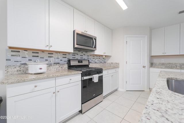 kitchen with stainless steel appliances, light tile patterned floors, light stone counters, backsplash, and white cabinets