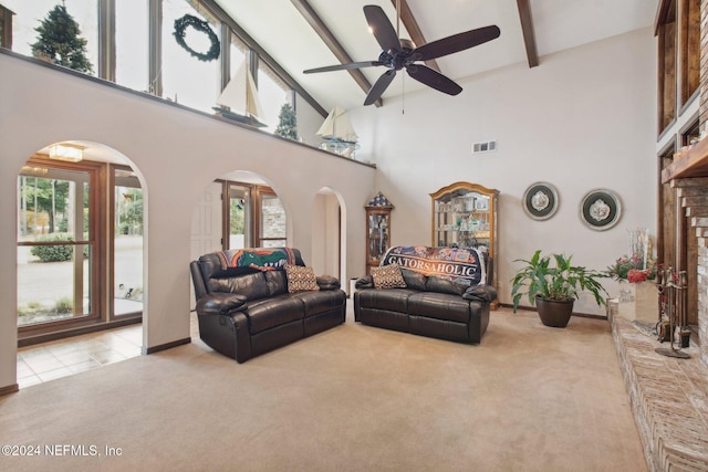 living room with a towering ceiling, ceiling fan, beamed ceiling, and light colored carpet